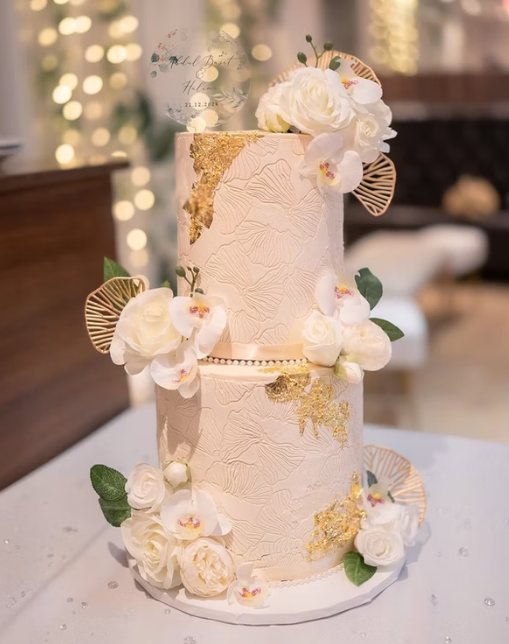Two-tier ivory and gold-leaf celebration cake decorated with white roses and orchids