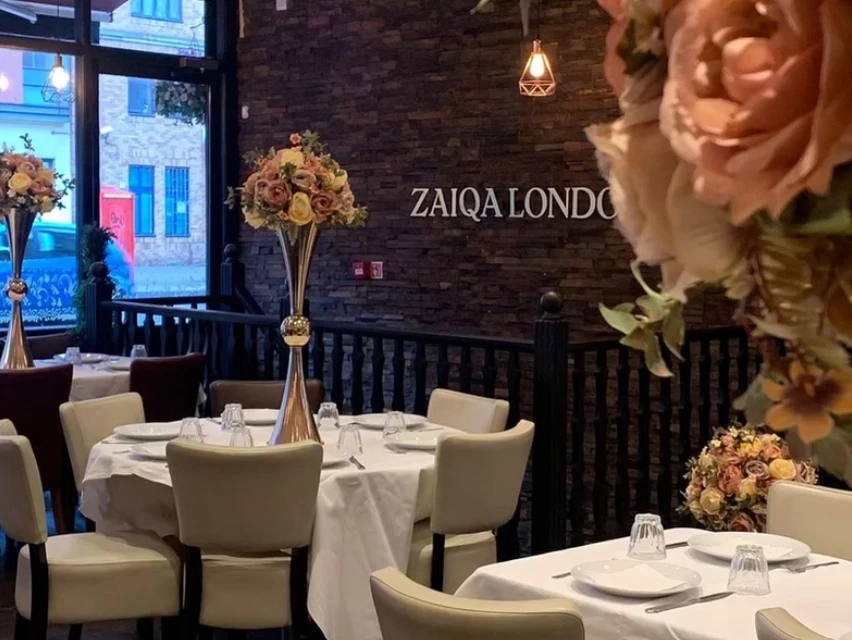 The dining room at Zaiqa London, with white tablecloths, gold floral centrepieces and the Zaiqa London sign on the brick wall